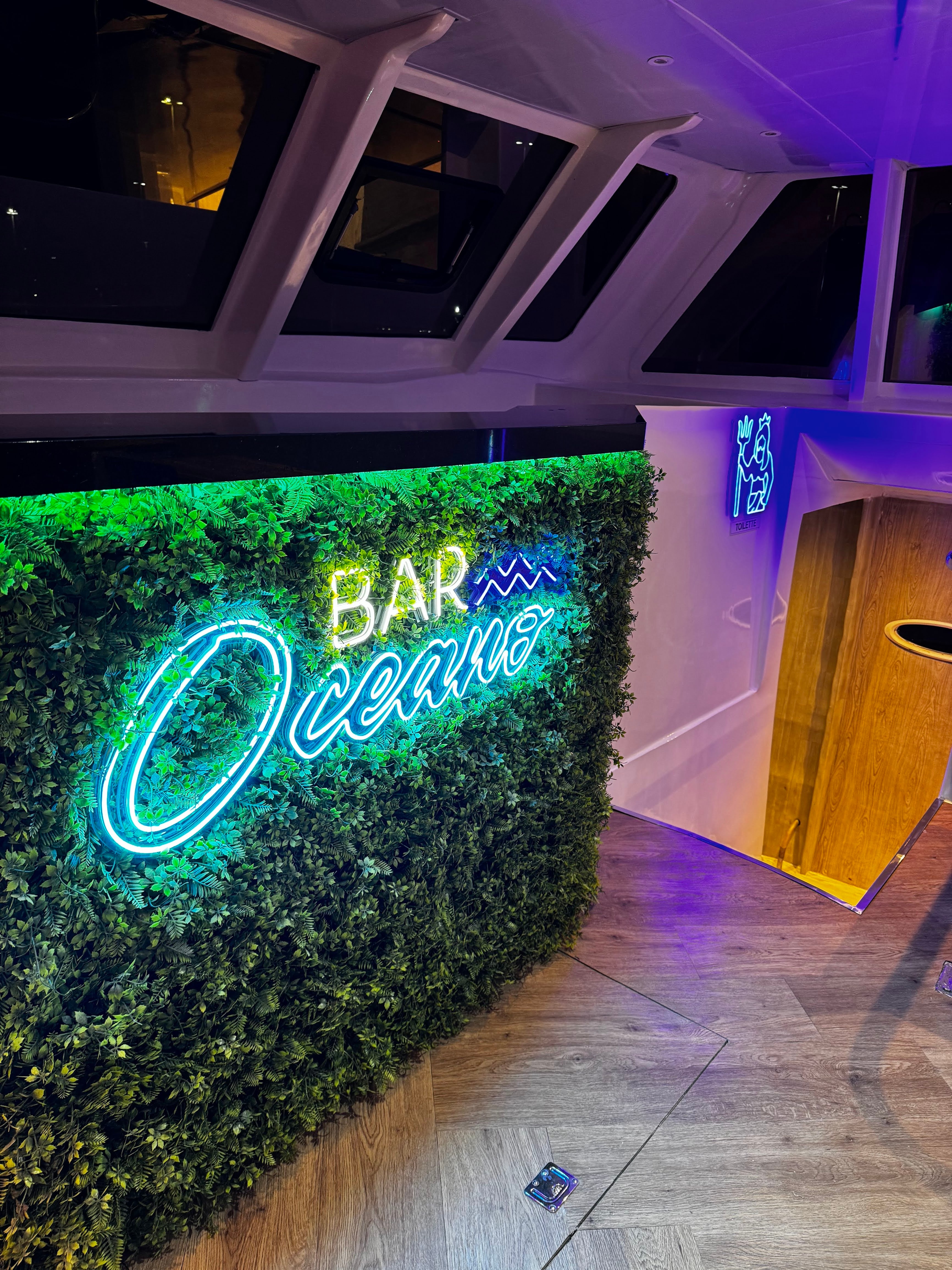 Bar Oceano neon sign on green plant wall inside the boat