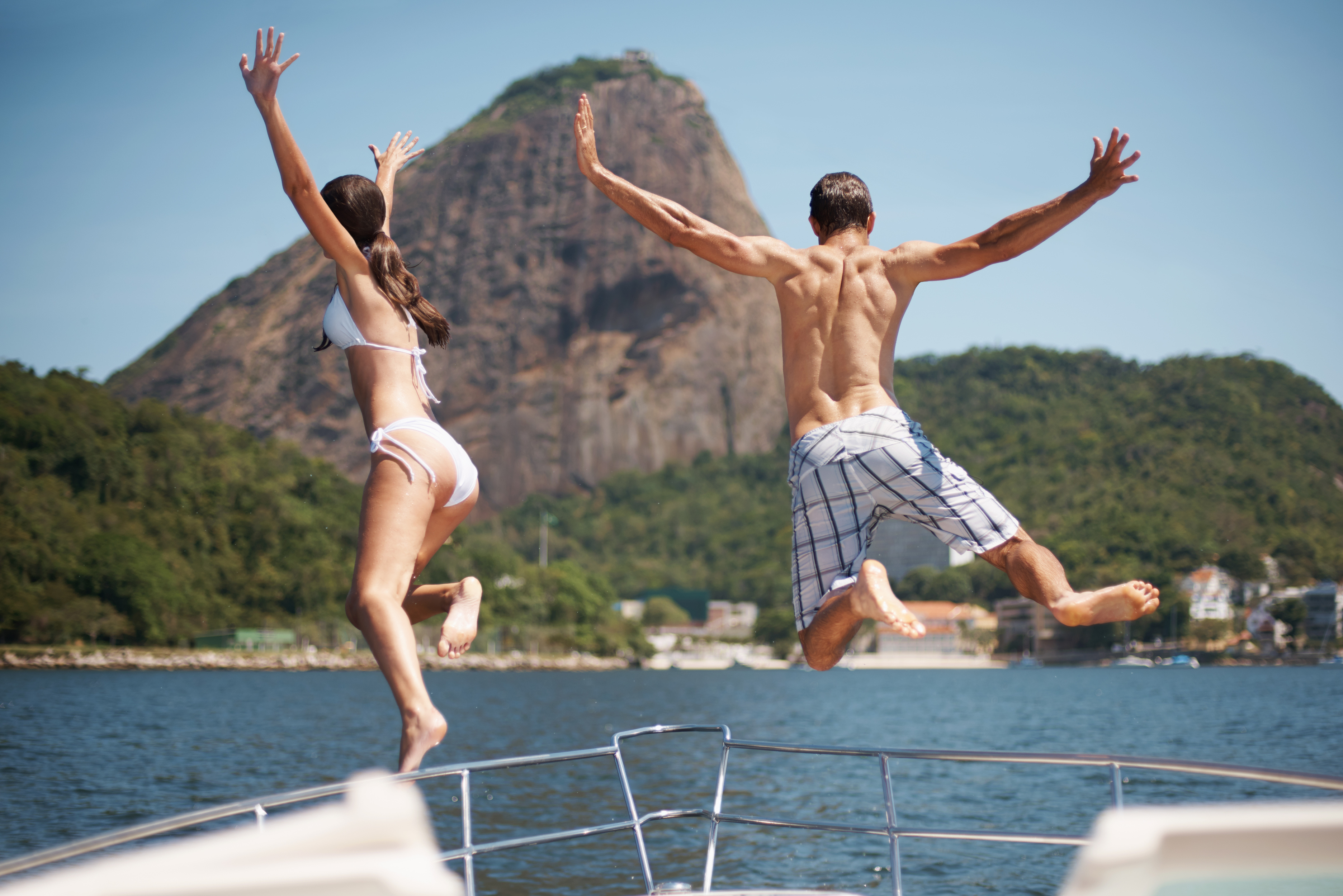 Casal pulando de iate com Pão de Açúcar ao fundo